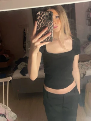 Svart croppad topp med öppen rygg - Snygg svart croppad topp med fyrkantig ringning och korta ärmar. Toppen har en cool öppen ryggdetalj som gör den extra trendig. Perfekt att styla med höga byxor eller kjol för en modern look.