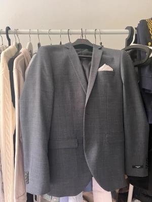 Grå kavaj från Jack & Jones - Snygg grå kavaj från Jack & Jones Premium med klassisk passform och två fickor framtill. Kavajen har en stilren design, smala slag och en bröstficka med vit näsduk. Perfekt för en dressad look. Byxorna som hör till är i ett annat inlägg 