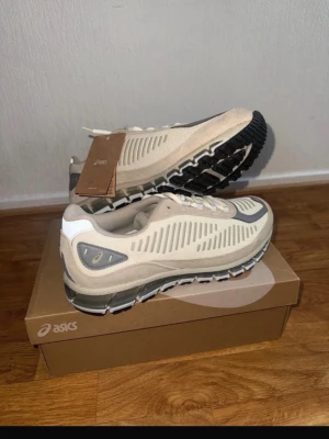 Beige ASICS sneakers med grå detaljer - Snygga sneakers från ASICS i beige mesh med grå och vita detaljer. Skorna har en chunky svart sula och stilrena linjer på ovandelen. Perfekta för dig som gillar en sportig och modern look. Klassisk snörning och bekväm passform.