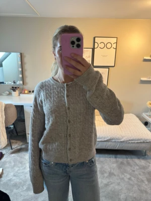 Grå kabelstickad kofta från H&M - Mysig grå/beige kabelstickad kofta från H&M med rund halsringning och knäppning framtill.❤️