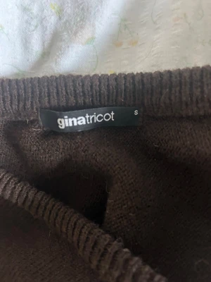 Brun kofta från Gina Tricot - Mysig brun kofta från Gina Tricot med v-ringning och knappar framtill. Koftan har långa, lite vidare ärmar och ribbade muddar vid ärmslut och midja. Perfekt att slänga över en topp för en chill look.