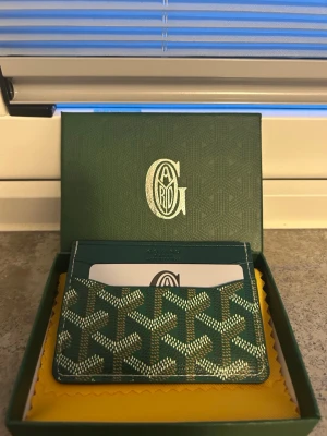 Grön korthållare - Snygg grön kortplånbok med klassiskt mönster i vitt och gult. Plånboken har flera kortfack och är tillverkad i exklusivt läder. Kommer i originalask med putsduk. Perfekt för dig som vill ha något stilrent och lyxigt i fickan.