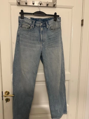Ljusblå raka jeans från H&M - Säljer ett par ljusblå jeans med loose passform från H&M. Klassisk femficksmodell med bälteshällor och knappgylf. Jeansen har en avslappnad vibe och är tillverkade i denim av bomull. Perfekta för en casual och trendig look. Storlek 30/32