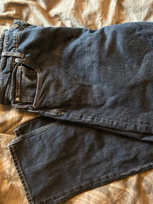 Mörkblå raka jeans - Säljer ett par mörkblå jeans med rak passform och klassisk femficksdesign. Jeansen har normal midja och är tillverkade i denim med synliga sömmar. Perfekta för en avslappnad och stilren look.