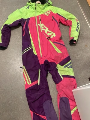 Färgstark täckbyxa från FXR - Säljer ett par riktigt färgstarka täckbyxor från FXR i neonrosa, limegrönt och lila. Byxorna har flera dragkedjor, fickor och coola detaljer. Perfekt för dig som vill sticka ut i backen och gillar sportig stil. Materialet är tåligt och vindtätt.