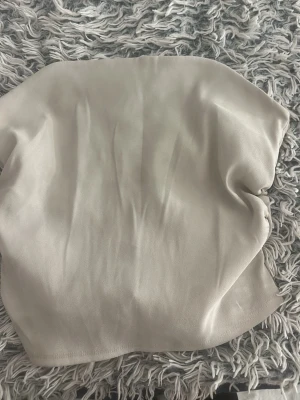 Beige axelbandslös tubtopp - Snygg beige tubtopp i mjukt material med enkel design. Toppen är axelbandslös och har en dragkedja baktill för enkel på- och avtagning. Perfekt att matcha med höga jeans eller kjol för en clean look.