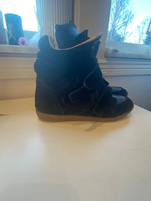 Svarta kilsneakers - Snygga svarta sneakers  med högt skaft och kardborreband. Skorna har en chunky sula i gummi och är tillverkade i mocka och läder. Perfekta för dig som vill ha en cool och trendig look. De är inte äkta Isabel marants, köpta för 2500kr