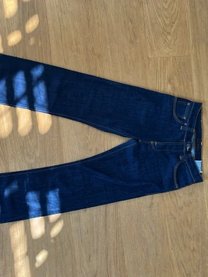 Mörkblå jeans från Nudie Jeans - Snygga mörkblå jeans från Nudie Jeans med klassisk femficksmodell och kontrastsömmar. Jeansen har rak passform och är tillverkade i denim med en tydlig struktur. Perfekta för dig som gillar stilrena och tidlösa jeans. Jeansen är i modellen average joe. Hör av er om ni har några funderingar!
