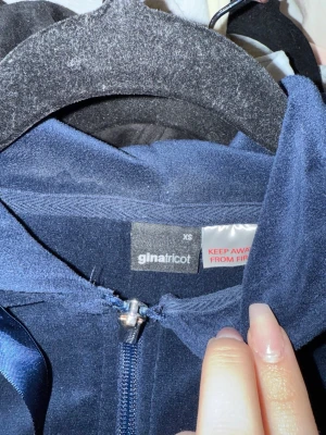 Mörkblå velourhoodie från Gina Tricot - Mjuk och skön mörkblå hoodie i velour från Gina Tricot. Hoodien har dragkedja framtill, långa ärmar och en stor huva. Perfekt för en chill och avslappnad stil. Materialet är lent och ger en snygg glansig look.