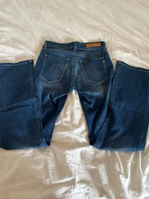Blå bootcut jeans från Replay - Säljer ett par blå bootcut jeans från Replay med klassisk femficksdesign och snygga slitningar. Jeansen har en läderpatch med Replay-logga bak i midjan och kontrastsömmar. Perfekta för en avslappnad och trendig look. Endast testade💕