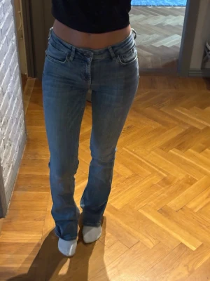 Blå bootcut jeans med låg midja - Snygga blå bootcut jeans med låg midja och klassiska fem fickor. Jeansen har en lätt tvättad look och är tillverkade i denim med lite stretch för skön passform. Perfekta för dig som gillar en avslappnad men trendig stil.