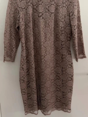 Pernilla Wahlgren, spetsklänning - Säljer en beige kortklänning i spets med trekvartsärm och snygg guldfärgad dragkedja bak. Klänningen har ett blommigt spetsmönster och är perfekt för dig som gillar romantisk stil. 