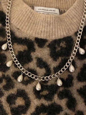 Silverfärgat halsband med pärldroppar - Snyggt halsband i silverfärgad rostfritt stål med sju droppformade pärlor som hänger längs kedjan. Perfekt för att ge din outfit en trendig och elegant touch. Kedjan har en chunky design och pärlorna är vita med fin glans.