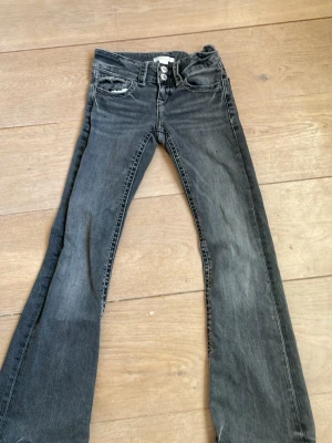 Svarta bootcut jeans Gina Tricot - Snygga svarta bootcut jeans från Gina Tricot med dubbla silverknappar och klassisk femficksmodell. Jeansen har en tvättad look och raka ben som går ut något nedtill. Perfekta för en trendig och avslappnad stil.