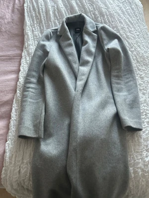 Ljusgrå kappa från Zara - Stilren ljusgrå kappa från Zara med klassisk krage och rak passform. Kappan är lång. 