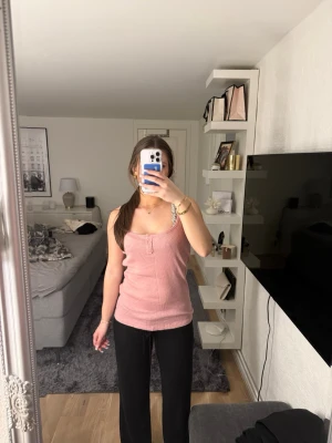 Rosa ribbad linnetopp med knappar - Säljer en ljusrosa ribbad linnetopp med smala axelband och dekorativa knappar framtill. Toppen har en figurnära passform och är perfekt för varma dagar. Liten logga nertill på sidan. Superenkel att styla till både jeans och kjol.