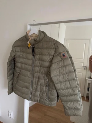 Olivgrön dunjacka khaki lättviktsjacka - Säljer en olivgrön jacka med quiltad design och hög krage. Jackan har två dragkedjeförsedda fickor, gul detalj vid halsen och klassisk logga på ärmen. Perfekt för kalla vinterdagar och riktigt snygg till streetwear. Finns bara lite smink fläckar på halsen men det går att tvätta bort enkelt 