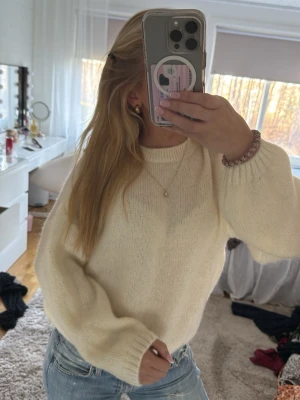 Krämvit stickad tröja med ballongärm - Mysig krämvit stickad tröja med ballongärmar och rund halsringning. Tröjan har en avslappnad passform och ribbstickade muddar vid ärmslut och nederkant. Perfekt för lager på lager och enkel att styla med jeans. Passar med allt.