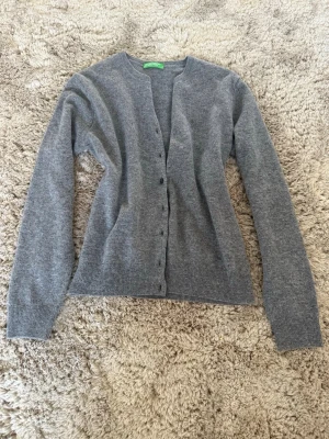 Grå basic kofta med knappar - En enkel och stilren grå kofta från United Colors Of Benetton med rund halsringning och knäppning framtill. Långärmad modell i mjukt material, perfekt att slänga över en t-shirt eller topp. Klassisk passform och ribbade muddar vid ärmslut och nederkant. Har aldrig använt🌸