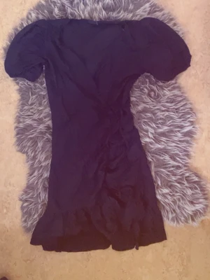 Svart kort puffärmad klänning - Snygg svart v-ringad kortklänning med puffärmar och lätt volang nertill. Klänningen har en figurnära passform och är perfekt för dig som gillar en trendig och stilren look. Passar till många olika tillfällen och är enkel att matcha med accessoarer.   