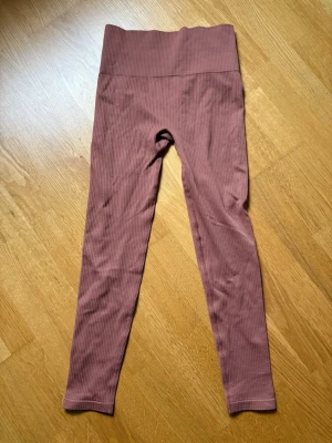 Rosa ribbade leggings från Röhnisch - Supersnygga ribbade leggings i dammig rosa nyans från Röhnisch. Hög midja och stretchigt material som sitter skönt och följsamt. Diskret ribbad struktur ger en trendig look och loggan syns framtill i midjan. Perfekta för dig som gillar både stil och komfort. Ny med prislapp!  Fint skick, oanvända.  Storlek M/L.  Material: 93% polyamid, 7% elastan.