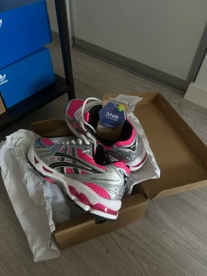 Asics Gel-kayano 14 neon rosa - Snygga Asics sneakers med mesh i stark rosa och silverfärgade detaljer. Skorna har vita snören, svart logga och svart insida. Sulan är vit med rosa och svarta inslag. Perfekta för dig som gillar sportig stil och vill sticka ut.