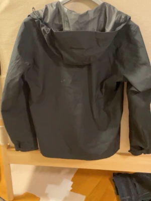 Uniqlo softshell jacka  - Snygg svart regnjacka från Uniqlo med dragkedja framtill och huva. Jackan har en minimalistisk design och är tillverkad i ett vattenavvisande material som passar perfekt för regniga dagar. Långa ärmar och enkel passform gör den både praktisk och stilren.