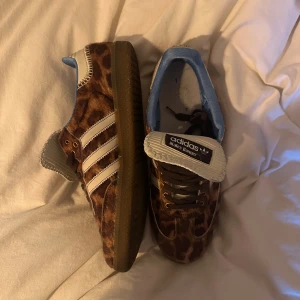 Adidas Wales Bonners - Unika Adidas sneakers med leopardmönster i brunt och beige, klassiska vita stripes på sidan och ljusblå detaljer vid hälen. Skorna har gummisula och snörning framtill. Perfekta för dig som vill sticka ut med din stil.