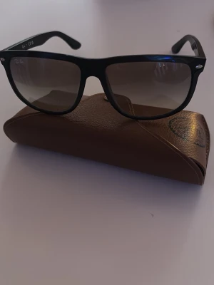 Svarta Ray-Ban Boyfriend solglasögon - Snygga svarta Ray-Ban Boyfriend solglasögon med mörka tonade glas. Kommer med brunt fodral i läderlook. Perfekta för soliga dagar och ger en cool vibe till din outfit.