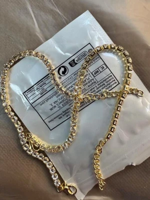 Guldarmband med glittrande stenar - Snyggt armband i guldfärg med gnistrande, klara stenar som ger en lyxig känsla. Armbandet har en klassisk tennisdesign och justerbar kedja för perfekt passform. Perfekt accessoar för att lyfta din outfit.