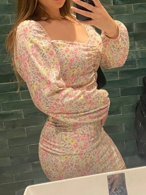Kortklänning med blommigt mönster - Kortklänning med blommigt mönster. Klänningen har puffiga långärmar, fyrkantig ringning och figurnära passform. Perfekt för vår och sommar. Materialet känns lätt och bekvämt.