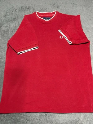 Fred Perry T-Shirt – Red – Size S - Klassisk t-shirt från Fred Perry i röd färg med vita kontrastdetaljer.  Minimalistisk design med den ikoniska laurel wreath-loggan på bröstet.  Perfekt till jeans eller shorts för en klassisk casual stil.  Detaljer • Fred Perry • Röd färg • Broderad logga • Kontrastdetaljer på ärmar och krage • Storlek S  📦 Skickas snabbt 💬 Hör av dig vid frågor