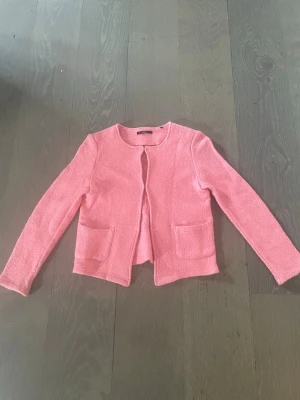 Rosa kofta från Zero med fickor - Söt rosa kofta från Zero med rund halsringning och två praktiska fickor framtill. Koftan är öppen framtill utan knappar och har långa ärmar. Materialet ser mjukt och lite fluffigt ut, perfekt för lager på lager och en chill look.