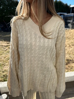 Beige kabelstickad tröja - Kabelstickad tröja i beige färg med v-ringning och avslappnad passform. Tröjan har långa ärmar och ribbade muddar vid ärmslut och nederkant. Perfekt för lager på lager och en chill look. 💕💕