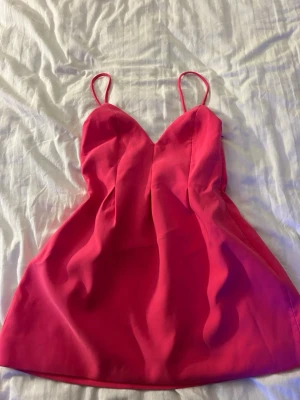 Rosa kort klänning från Zara - Säljer en snygg rosa kort klänning från Zara med tunna axelband och v-ringad urringning. Klänningen har en enkel, figurnära passform och är perfekt för varma dagar. Använd en gång