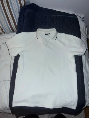 Vit piké från New yorker - Klassisk vit pikétröja med korta ärmar och snygg krage. Materialet har en strukturerad yta som ger en modern känsla. Perfekt till jeans eller shorts för en clean look.