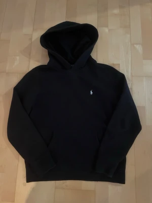 Svart hoodie från Polo Ralph Lauren - Snygg svart hoodie från Polo Ralph Lauren med klassisk huva och liten broderad logga på bröstet. Tillverkad i mjukt material som känns skönt mot huden. Perfekt för en avslappnad och stilren look. Skick 9/10 riktig bra skick! Storlek XS! Skriv till mig vid intresse eller frågor!