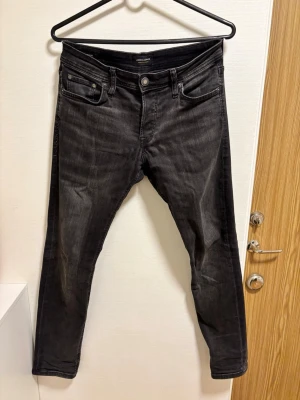 Svarta slim fit jeans från Jack & Jones - Snygga svarta slim fit jeans från Jack & Jones med klassisk femficksdesign och diskreta slitningar. Jeansen har normal midja och smal passform som ger en modern look. Tillverkade i stretchigt denim för extra komfort.