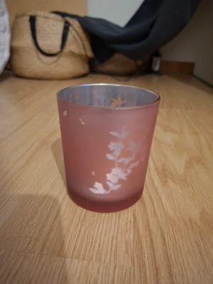 Rosa glaslykta med blommönster - Säljer en rosa glaslykta med frostad yta och vitt blommönster. Perfekt som ljuslykta eller dekoration i rummet. Glaset har en mjuk, rund form och ett subtilt mönster som ger mysig känsla.