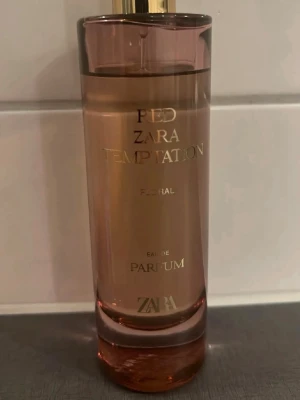 Zara Red Temptation Parfym - Zara Red Temptation är en elegant parfym i en cylinderformad glasflaska med rosaröd ton och guldfärgad text. Flaskan har en stilren design och lock i guld. Doften är floral och passar dig som gillar lyxiga och moderna parfymer.