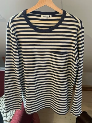 Randig långärmad tröja Weekday - Snygg långärmad tröja från Weekday med marinblå och vita horisontella ränder. Tröjan har en rund halsringning med bredare kant och en liten bröstficka på vänster sida. Perfekt för en avslappnad och stilren look. Storlek M men passar även L.