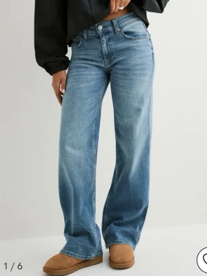 Blåa vida jeans med låg midja - Säljer ett par blåa jeans med hög midja och raka, vida ben. Jeansen har klassisk femficksdesign och ljus tvätt med subtila slitningar. Perfekta för en avslappnad och trendig look. Materialet är mjuk denim i bomull. Storlek 32/short, perfekt i längden för mig som är 160 cm. Aldrig använda, prislapp kvar