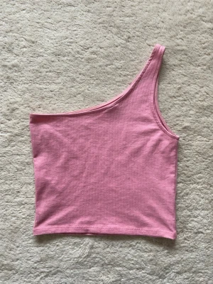 Rosa ribbad oneshoulder topp - Snygg rosa ribbad topp med oneshoulder-design. Perfekt för dig som vill ha en enkel men snygg look. Materialet är mjukt och stretchigt, vilket gör toppen bekväm att bära. Passar perfekt till både jeans och kjol.