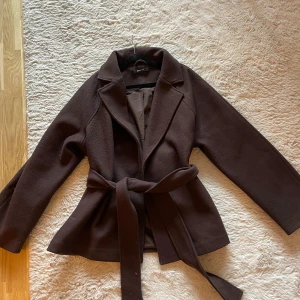 Brun kappa med knytskärp - Stilren brun kappa från Gina Tricot med bred krage och knytskärp i midjan, lite nopprig