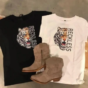 Reckless t-shirt med tiger från Prepair - Cool t-shirt från Prepair med tryck av en tiger och texten 'RECKLESS' på framsidan. Finns i både svart och vitt. Klassisk rund halsringning och korta ärmar. Tillverkad i mjuk bomull som är skön mot huden. Perfekt för dig som vill sticka ut med ett djurmotiv. Vit i storlek M .  Svart storlek XS . Priset är för 1 st 