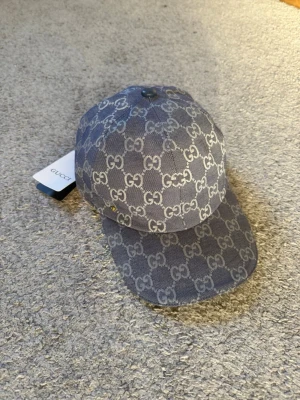 Gucci  - Snygg keps från Gucci i blått tyg med det klassiska GG-monogrammet i vitt över hela kepsen. Böjd skärm och justerbar passform. Märkets logotyp syns tydligt och kepsen har en modern streetwear-vibe. Perfekt för dig som vill sticka ut med exklusiv stil.
