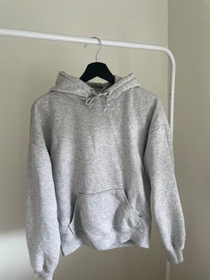 Grå basic hoodie med ficka - En enkel och stilren grå hoodie med huva och dragsko. Hoodien har en stor känguruficka framtill och ribbade muddar vid ärmar och nederkant. Perfekt oversized passform för en avslappnad look. Tillverkad i mjukt sweatshirtmaterial.