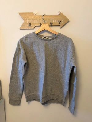 Grå basic sweatshirt utan huva från primemark - En enkel och stilren grå sweatshirt i mjukt material med rund halsringning och ribbade muddar vid ärmslut. Perfekt för en avslappnad och bekväm look. Passar till det mesta och är lätt att matcha med andra plagg.