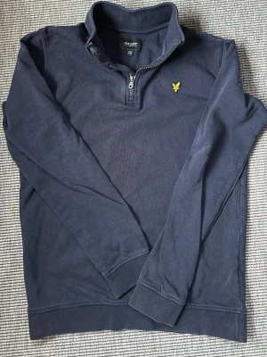 Lyle & Svott - Mörkblå half-zip tröja junior - Mörkblå långärmad junior tröja från Lyle & Scott med half-zip och ståkrage. Storlek 12/13 years står det i kragen. Jag anser att den är liten i storleken, obs juniortröja. Tröjan har det klassiska gula logobroderiet på bröstet och är tillverkad i mjuk bomull. Perfekt för en avslappnad men snygg stil. Nypris ca 700kr, säljes för 350kr. 