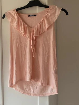 Ljusrosa volangtop från Gina Tricot - Supersöt ljusrosa topp från Gina Tricot med volangdetalj längs ringningen. Toppen är ärmlös och har en mjuk, flowy passform som känns riktigt somrig. Perfekt att styla med jeans eller kjol för en fräsch look. Har inte använt toppen själv men köpte på Vinted. Storlek XS. Har katter hemma!!!